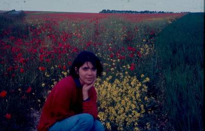 [Clarice Herzog agachada, tendo ao fundo flores amarelas e vermelhas]