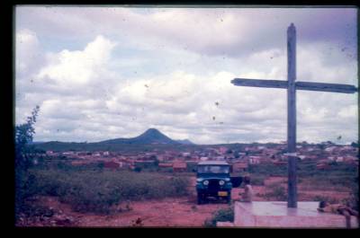 [Cruz, jipe e monte ao fundo]